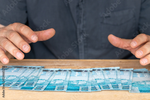 a man reaching for money spread on a desk, A large amount, Brazilian finances, banknotes for 100 reais, The concept of financial success, winning or a successful financial investment