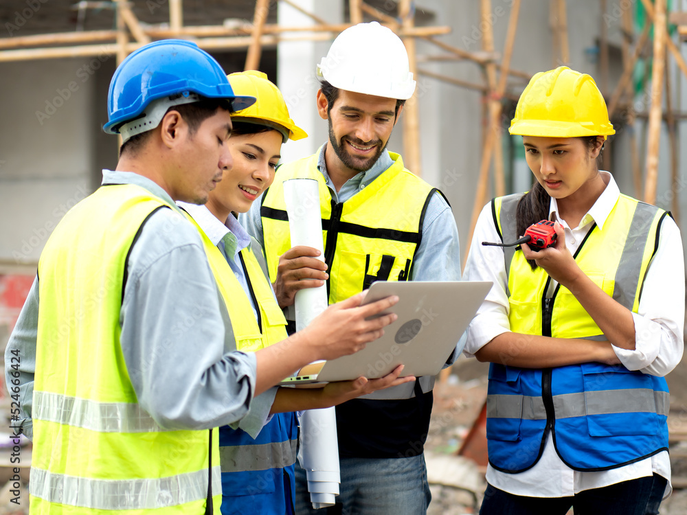 Construction engineer holds computer laptop meeting with architect teamwork. Multiracial people wear safety hats using laptops to discussion, brainstorm on housing development at construction site. Construction engineer holds computer laptop meeting with architect teamwork. Multiracial people wear safety hats using laptops to discussion, brainstorm on housing development at construction site.