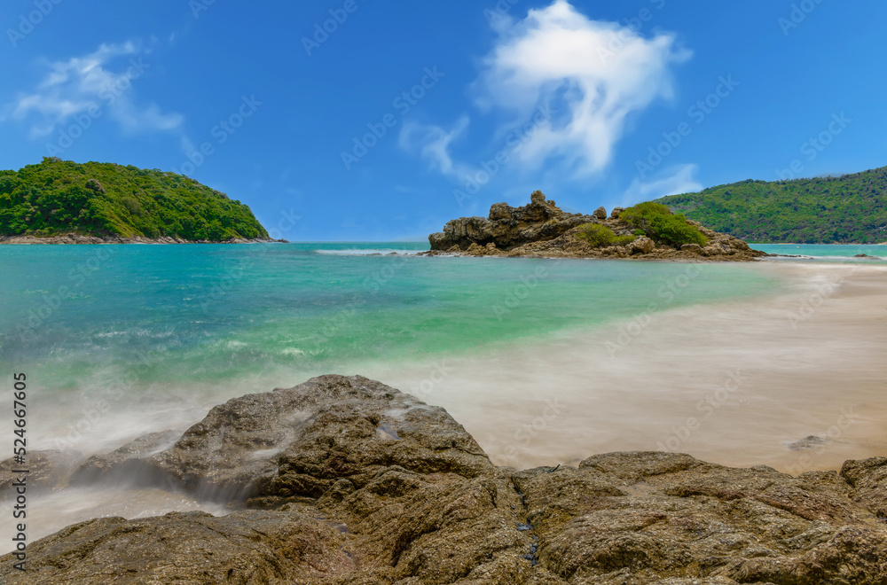 Fototapeta premium Long exposure of waves crashing on the rocks with beautiful island and mountains in Background. photographed in Naiharn Nai Harn Beach Phuket Thailand