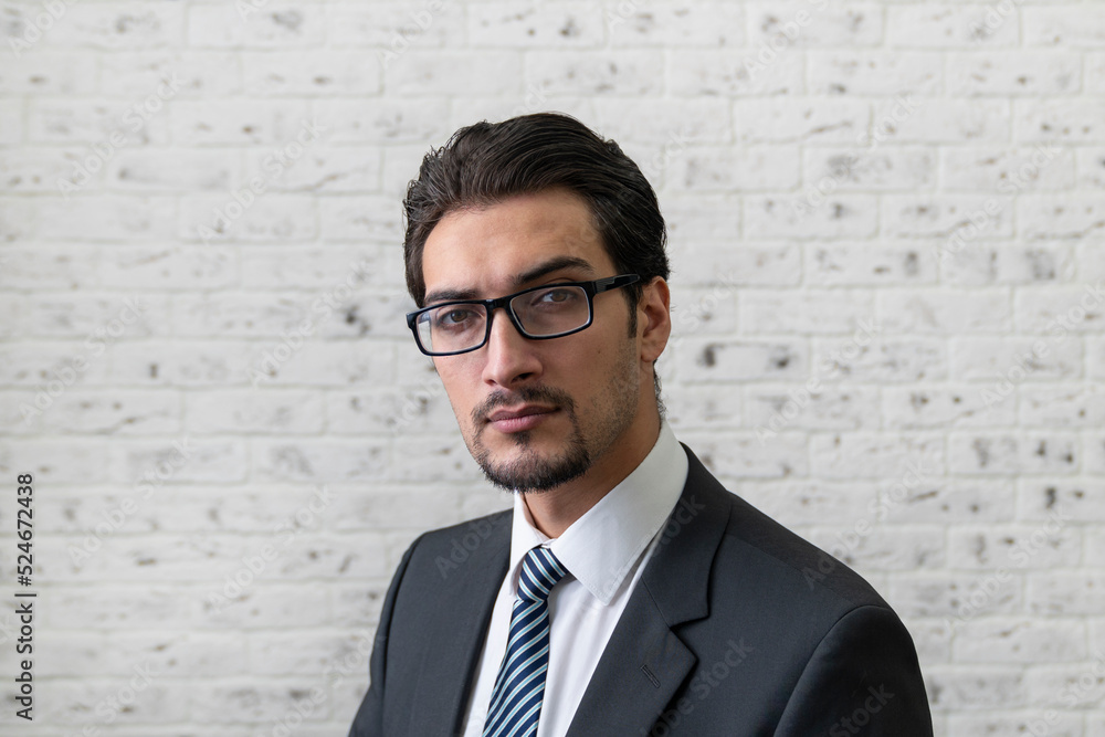 Close up portrait of handsome serious businessman in black suit and glasses on white brick wall background Close up portrait of handsome serious businessman in black suit and glasses on white brick wall background