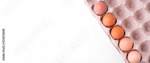 Web banner with raw chicken eggs with different eggshell shades in the carton box. Mockup with copy space on white photo