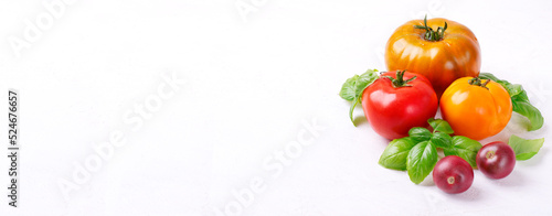 Web banner with assorted multicolored tomatoes and basil on white table. Food background. Mockup with copy space