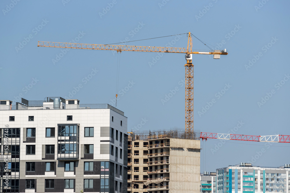 Yellow construction tower crane against the background of multi-apartment residential buildings under construction Yellow construction tower crane against the background of multi-apartment residential buildings under construction