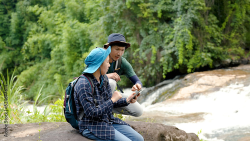 Asian man and woman couple are exploring routes and maps from their tablet to prepare a path to walk in the forest to their destination for a weekend getaway after a hard day at work.