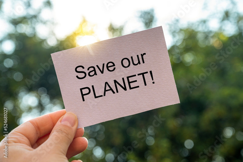 Save our planet words, written on white paper poster in female hand over green bokeh background. Save planet, climate changes concept © Inga