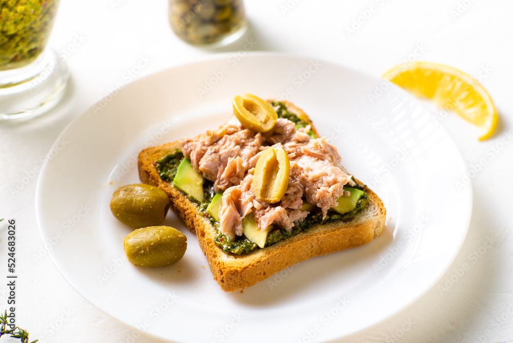 toast with tuna and avocado, olives with chimichurri sauce. On a white plate and white background.