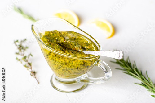 Chimichurri sauce in a gravy bowl on a white background. Argentinean vegetarian sauce made from olive oil, oregano, parsley.