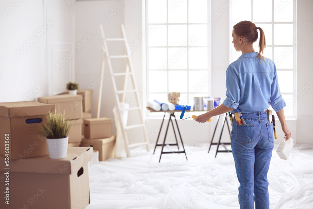 Happy woman paints wall with roller at home