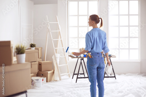 Happy woman paints wall with roller at home