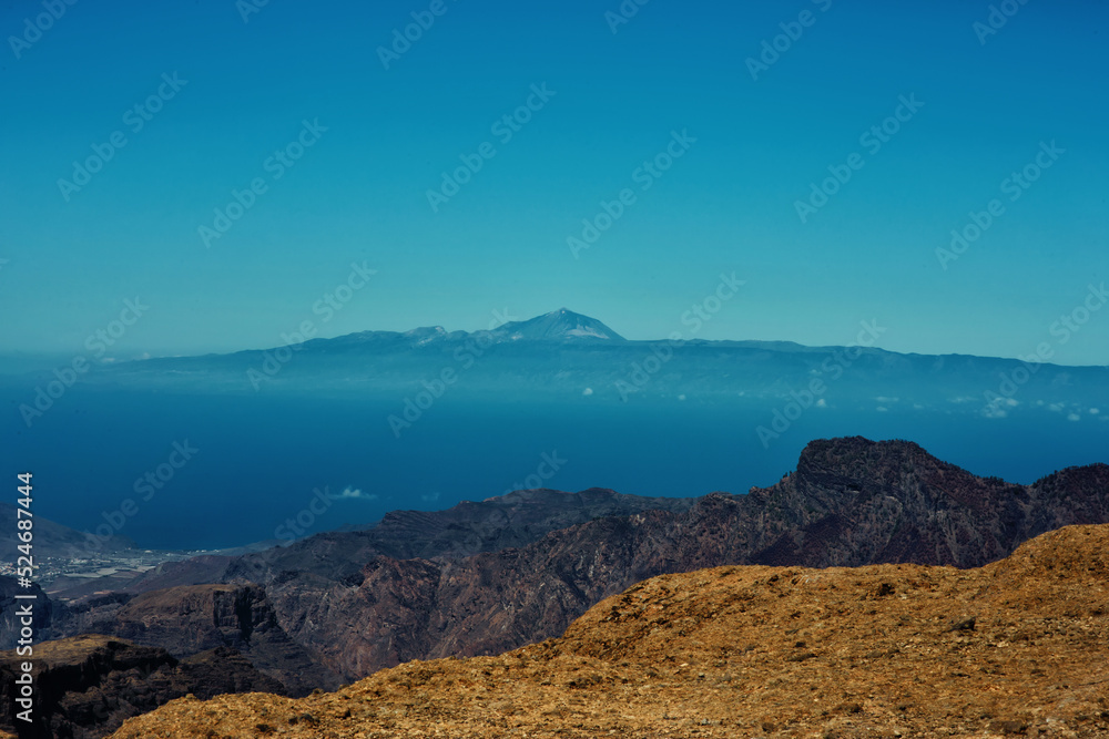 Edge of mountains on the island Gran Canaria with sky, neighboring island Tenerife and volcano Tejde on the background Edge of mountains on the island Gran Canaria with sky, neighboring island Tenerife and volcano Tejde on the background