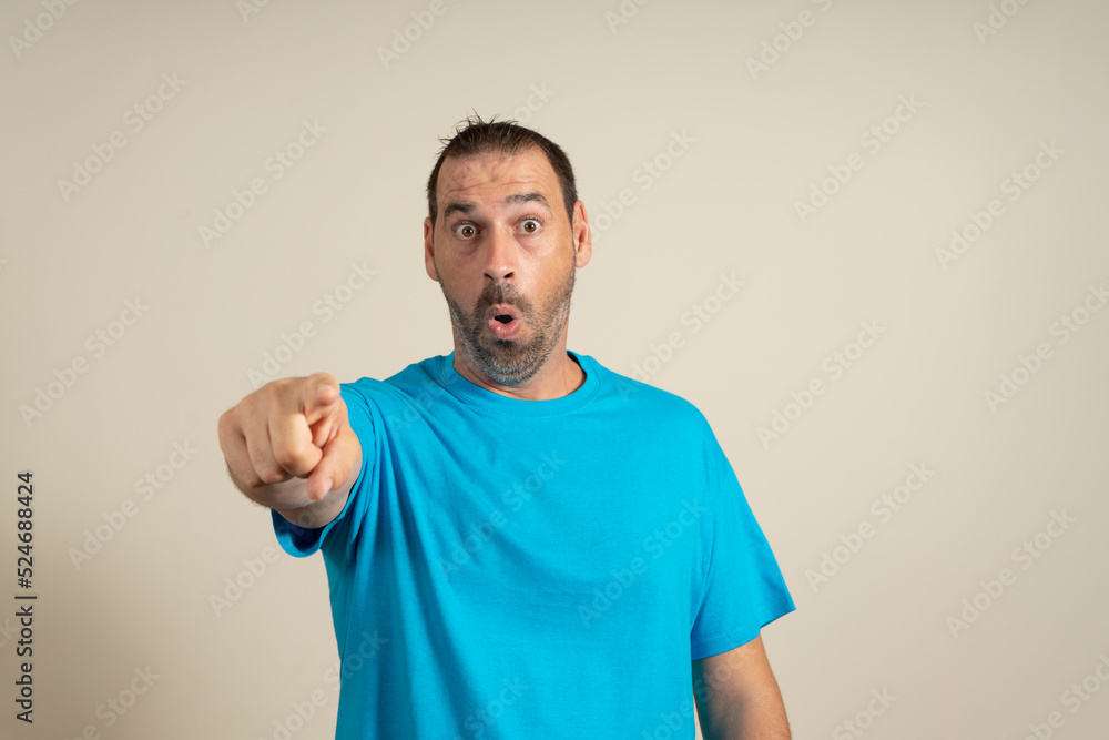 Bearded latin man in blue t-shirt pointing his finger at you camera gesture isolated on beige wall background Bearded latin man in blue t-shirt pointing his finger at you camera gesture isolated on beige wall background