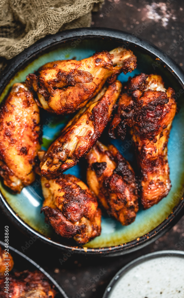 Close up of Roasted chicken wings on rustic ceramic plate over dark background Close up of Roasted chicken wings on rustic ceramic plate over dark background