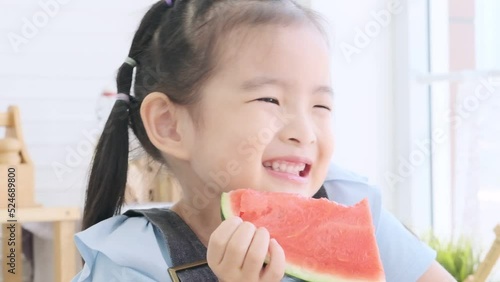 Cute asian little girl eating fresh watermelon deliciously in the kitchen.