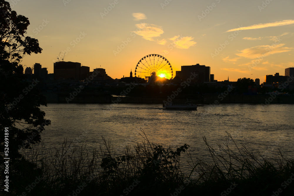 Montreal Grand Ferris Wheel in Old Port at sunset. Reflections of sun rays on Saint Laurent river with a background of cloudy blue sky
