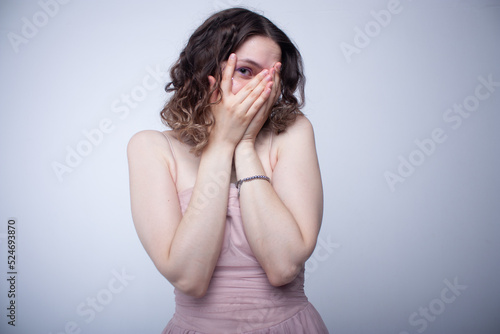 Portrait of a young girl holding her hands to her face and peeping. White background