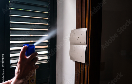 hand using mosquito insecticide spray to kill flies and mosquitoes. clearly visible backlight spray with droplets.