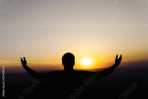 Sunset with a silhouette of a young man in an attitude of gratitude to the sun photo