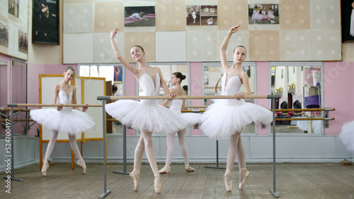 in the ballet hall, girls in white ballet tutus, packs are engaged at ballet, rehearse croise forward, Young ballerinas standing on toes in pointe shoes at railing in ballet hall. High quality photo photo