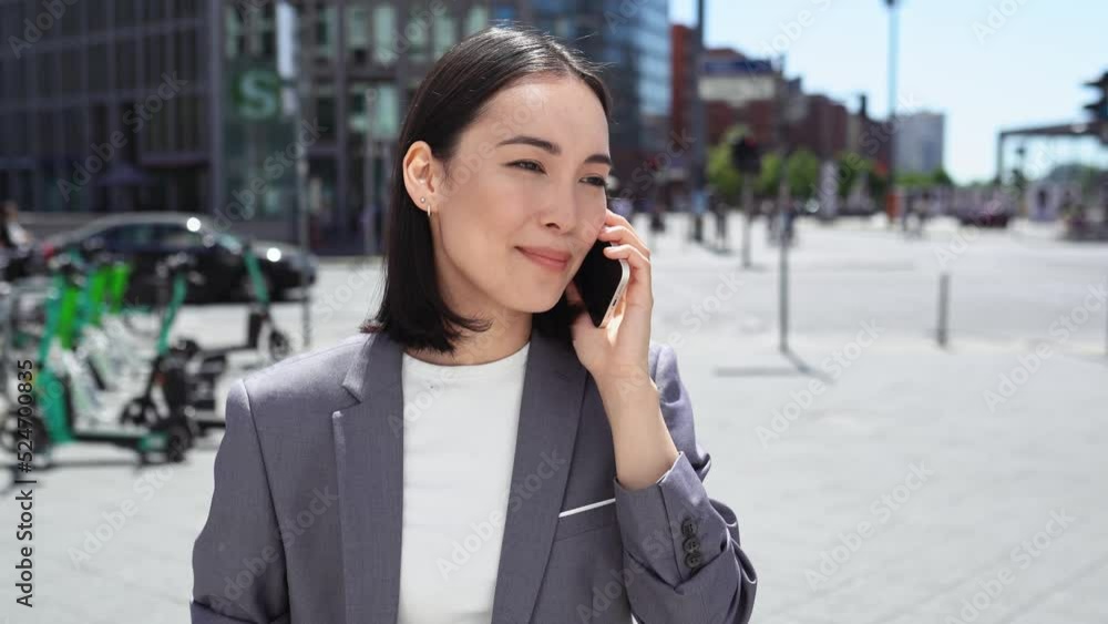 Young busy professional Asian business woman professional manager executive wearing suit making call on cellular holding mobile phone talking to client by cellphone standing on urban big city street. Young busy professional Asian business woman professional manager executive wearing suit making call on cellular holding mobile phone talking to client by cellphone standing on urban big city street.