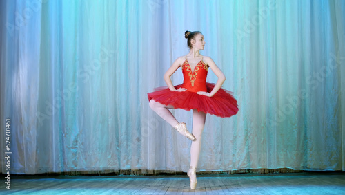 ballet rehearsal, on the stage of the old theater hall. Young ballerina in red ballet tutu and pointe shoes, dances elegantly certain ballet motion, pas courru , tour fouette. High quality photo photo