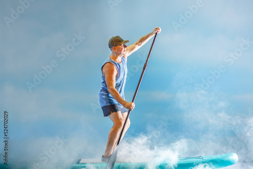 A man on a sub-board with an oar paddles in thick fog against the background of clouds.