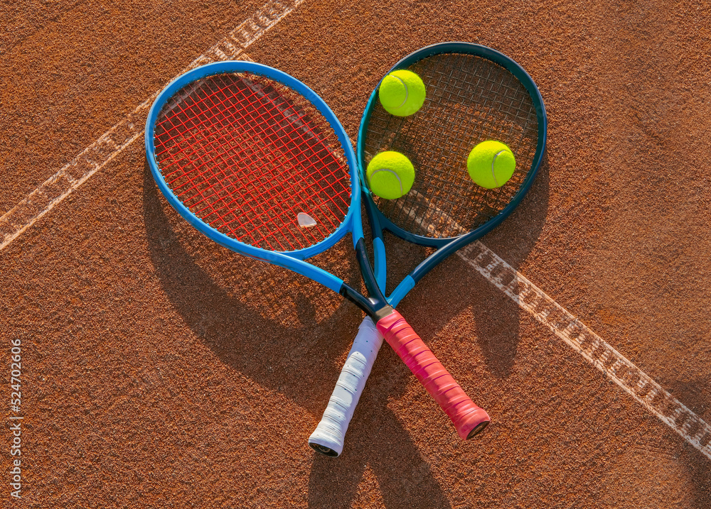 Two crossed tennis rackets with balls on a clay court