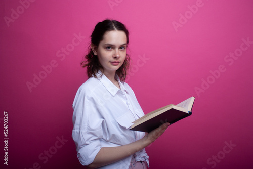 Portrait of a young girl standing with a book and looking into the camera.