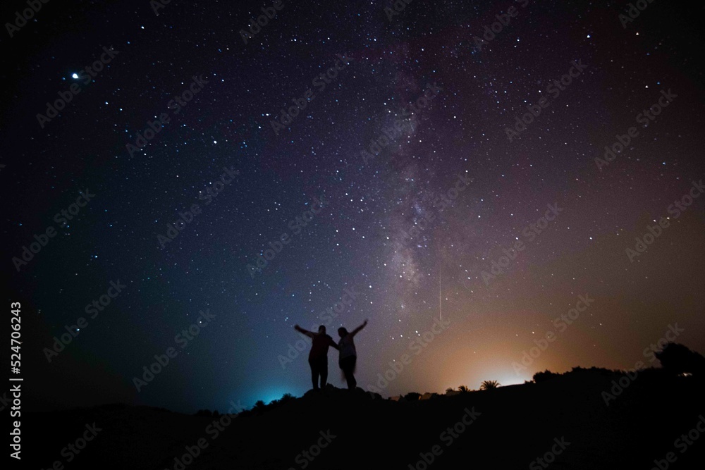 Milky Way. Night sky with stars and silhouette of a standing happy couple with yellow and blue light. Space background, Astro photography
