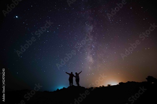 Milky Way. Night sky with stars and silhouette of a standing happy couple with yellow and blue light. Space background  Astro photography