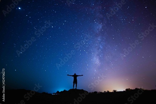 Milky Way. Night sky with stars and silhouette of a standing happy person with yellow and blue  light. Space background, Astro photography
