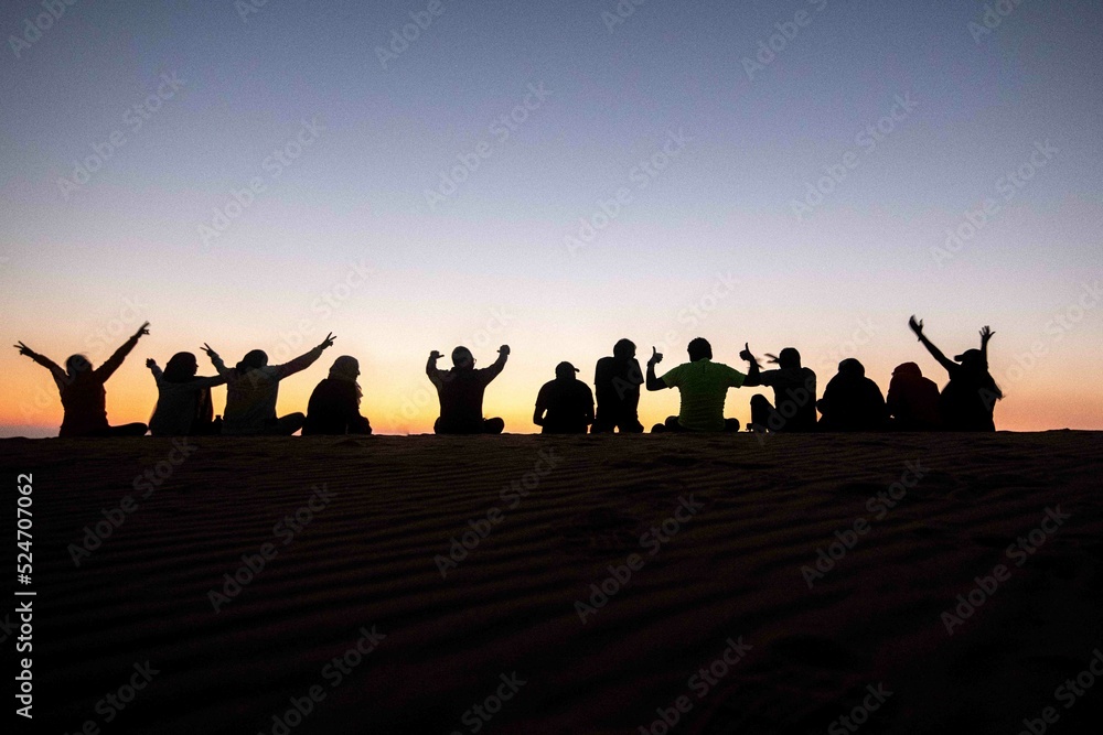 A group of people, team work, companions, friends sitting together during sunrise or sunset, silhouette