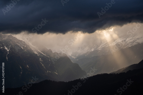 Sunrays coming from dark stormy clouds over Himalayan mountains during sunset. Rays of golden light shining through dark clouds. Sunset in mountain. Indian Himalayas