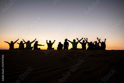 A group of people  team work  companions  friends sitting together during sunrise or sunset  silhouette