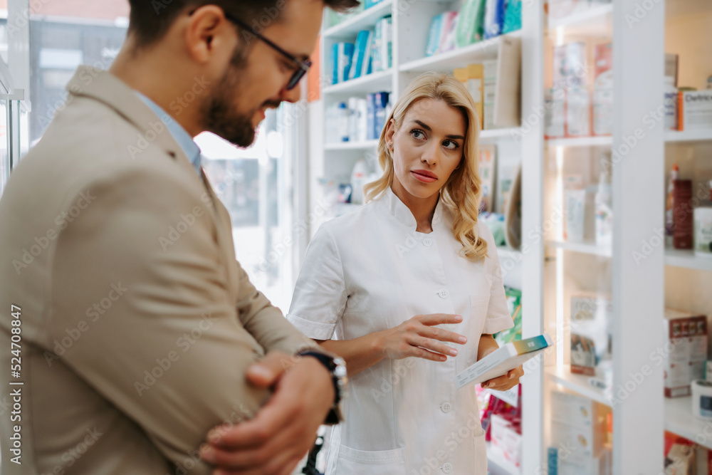Obraz premium Young business man choosing and buying drugs in a drugstore while talking with attractive female pharmacist. She helping him with expert advice.