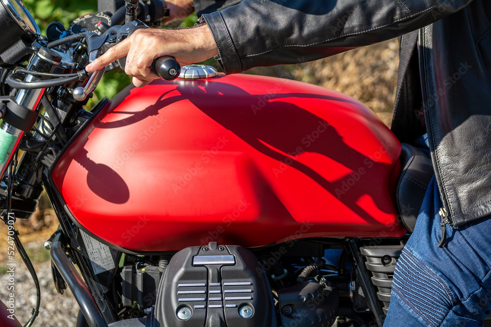 Détail de moto, réservoir rouge, moteur et accélérateur, main et blouson de cuir Détail de moto, réservoir rouge, moteur et accélérateur, main et blouson de cuir