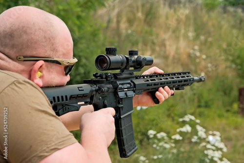 a man is holding an automatic weapon. a man looks into the sight of a military weapon.