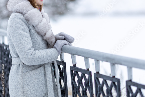 girl with warm winter clothes stands near the fence, winter snow and cold photo