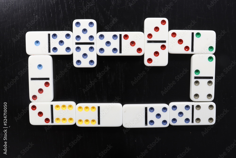 White domino pieces with colored dots over a black wood table White domino pieces with colored dots over a black wood table