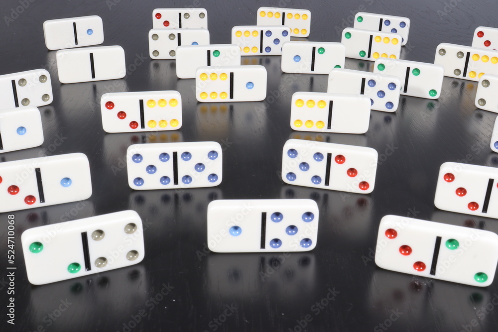 White domino pieces with colored dots over a black wood table White domino pieces with colored dots over a black wood table
