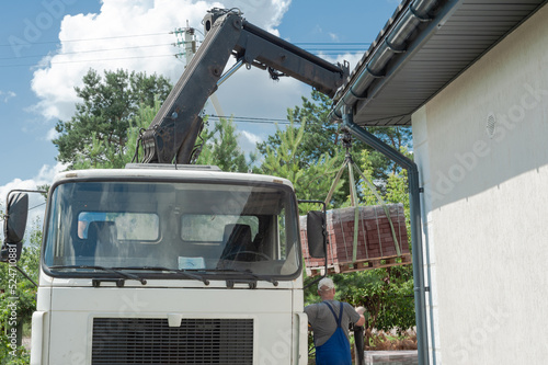 Unloading paving slabs from a truck. Men unload paving slabs using a manipulator. Workers unload building materials from a large machine.