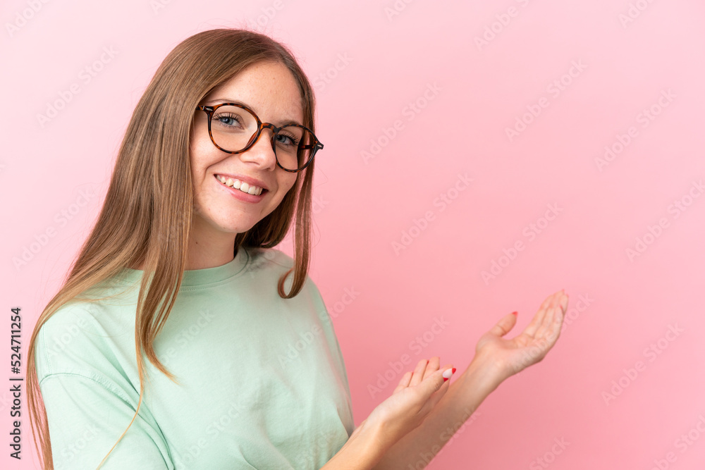 Young Lithuanian woman isolated on pink background With glasses and presenting something Young Lithuanian woman isolated on pink background With glasses and presenting something
