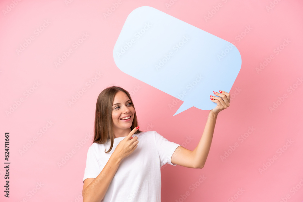 Young Lithuanian woman isolated on pink background holding an empty speech bubble and pointing it Young Lithuanian woman isolated on pink background holding an empty speech bubble and pointing it