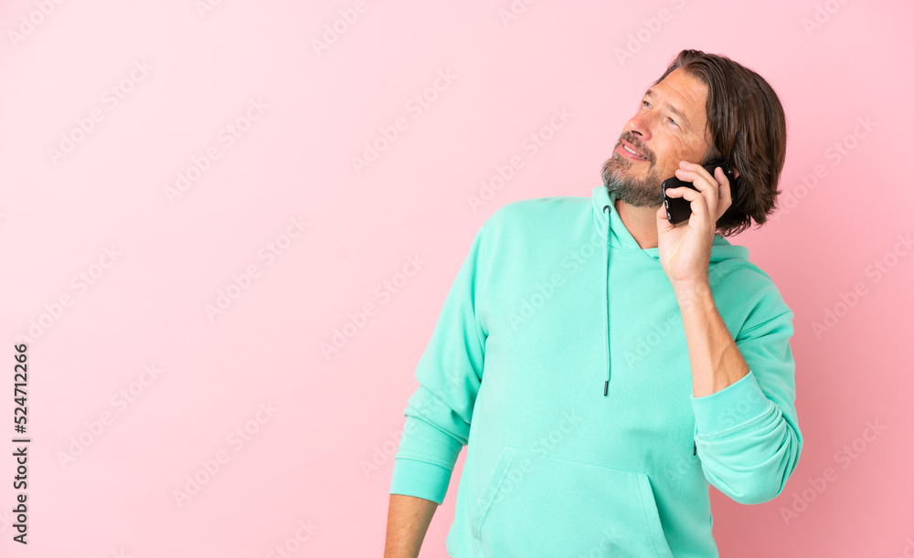 Senior dutch man isolated on pink background keeping a conversation with the mobile phone Senior dutch man isolated on pink background keeping a conversation with the mobile phone
