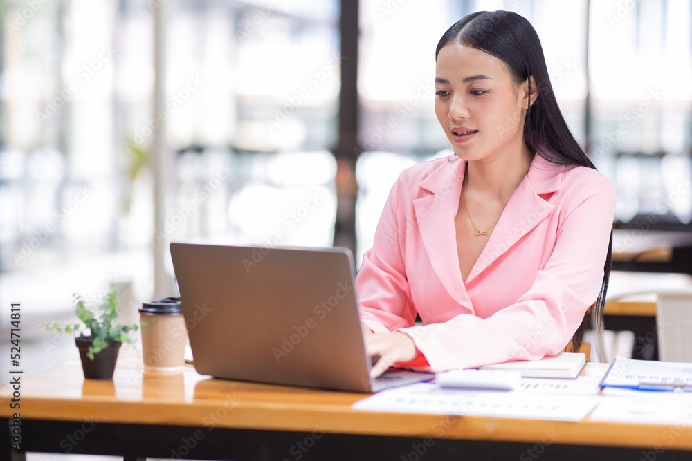 Asian Businesswoman Using a laptop computer and working at office with calculator document on desk, doing planning analyzing the financial report, business plan investment, finance analysis concept. Asian Businesswoman Using a laptop computer and working at office with calculator document on desk, doing planning analyzing the financial report, business plan investment, finance analysis concept.