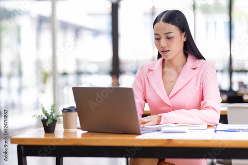 Asian Businesswoman Using a laptop computer and working at office with calculator document on desk, doing planning analyzing the financial report, business plan investment, finance analysis concept.