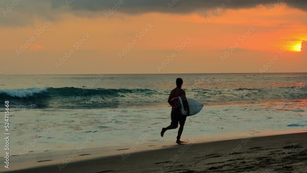 Young male surfer athlete run with surfboard on sandy beach on Bali island sea coast at sunset slow motion video backgroud Young male surfer athlete run with surfboard on sandy beach on Bali island sea coast at sunset slow motion video backgroud