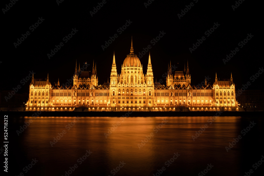 Naklejka premium Hungarian Parliament Building or Országház in front of the Danube river at night. Beautiful night landscape with an illuminated monument. Summer landscape scene from the city of Budapest, Hungary