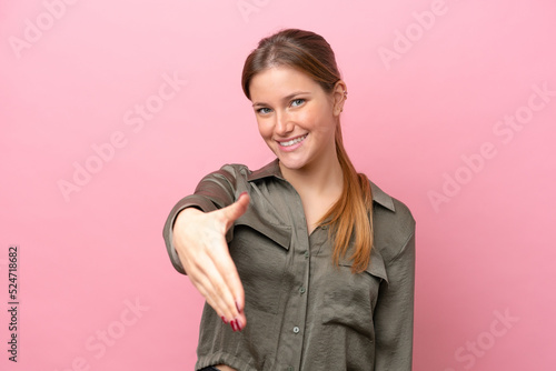 Young caucasian woman isolated on pink background shaking hands for closing a good deal