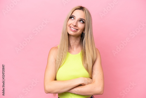 Pretty blonde woman isolated on pink background looking up while smiling