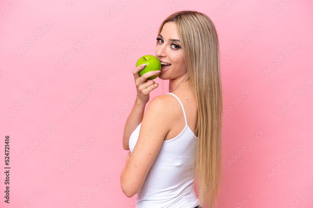 Pretty blonde woman isolated on pink background eating an apple Pretty blonde woman isolated on pink background eating an apple